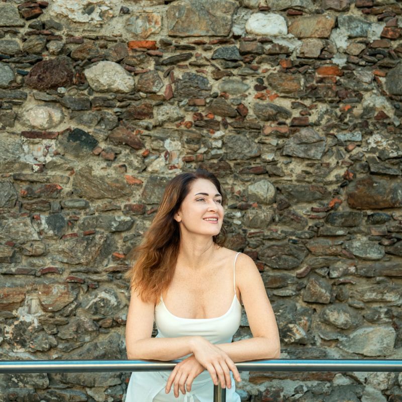 Contemplative woman posing by rustic stone wall in sunlit outdoor scene