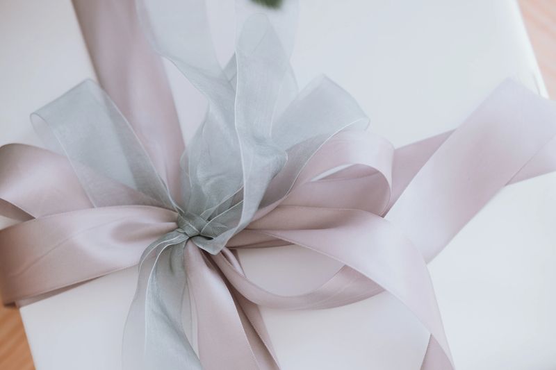 A beautifully wrapped gift box sits on a wooden surface, adorned with a delicate gray ribbon. The soft colors create a warm and inviting atmosphere, perfect for any occasion.