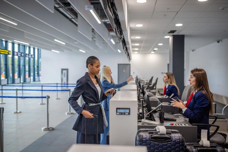 An airport check-in area bustling with travelers interacting with airline staff at the counter, with suitcases lined up and a dynamic travel environment on display.