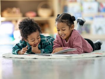 Two young children happily reading a book together on the floor.