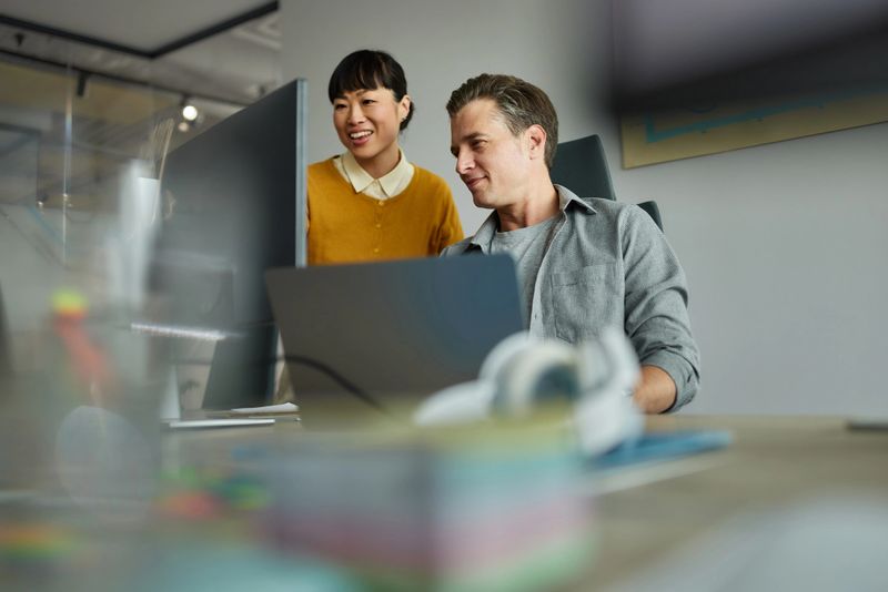 Below view of happy programmers cooperating while reading codes on desktop PC in the office. Focus is on man.