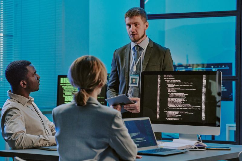 Group of three diverse young people discussing issues during meeting in modern cybersecurity department office