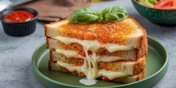 Triple-layer grilled cheese sandwich with melted cheese and basil.