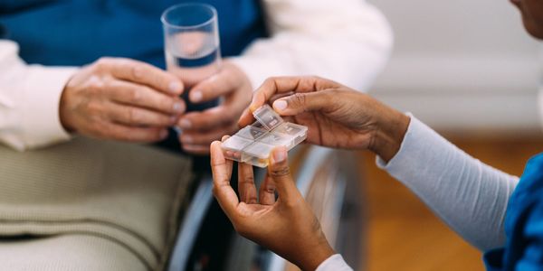 Two sets of hands. One is holding a medication container out. The other is holding a glass of water