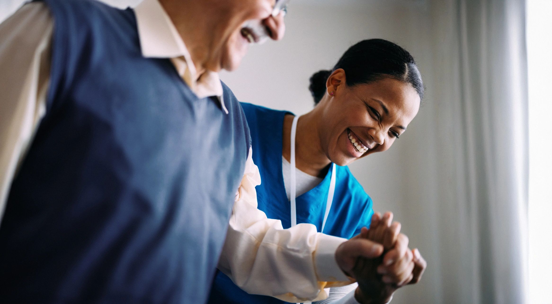 Caregiver joyfully assisting elderly man.