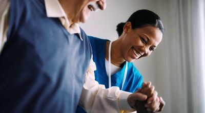 Caregiver smiling with elderly man, holding his hand.