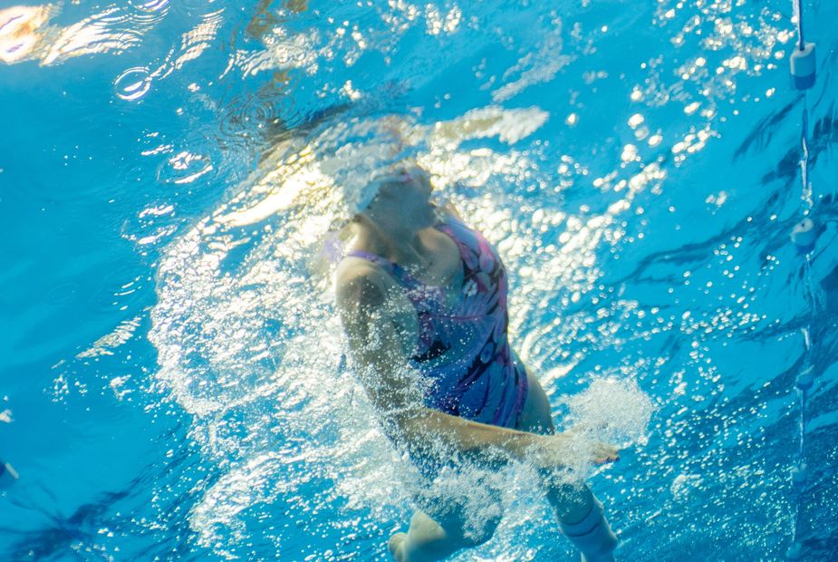 Artistic swimmers in training with focused coaches by the poolside.