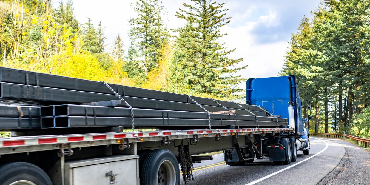 Blue truck carrying long metal beams on a highway.