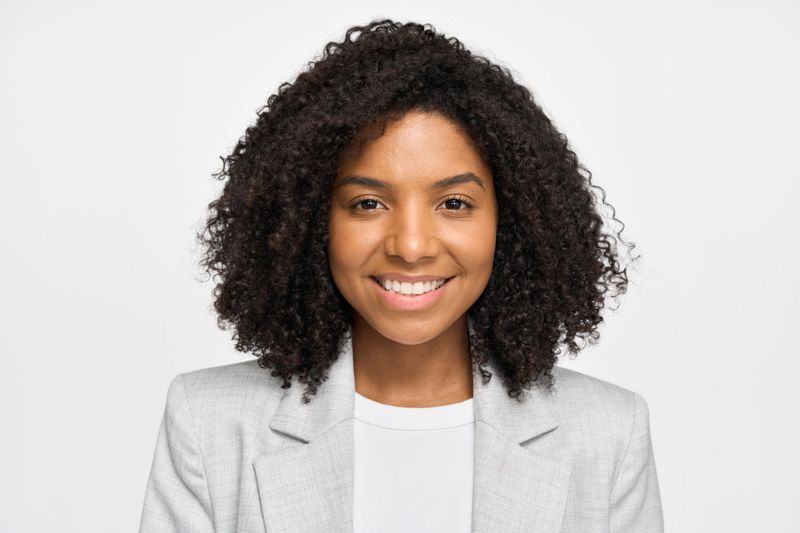 Happy confident young African American business woman standing isolated on white wall. Smiling professional businesswoman model wearing suit looking at camera, headshot close up portrait.