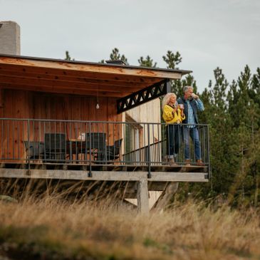 Elderly couple enjoying binocular views from a wooden cabin balcony.