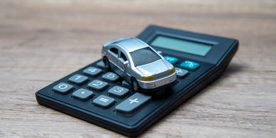 Toy car placed on a black calculator on a wooden surface.