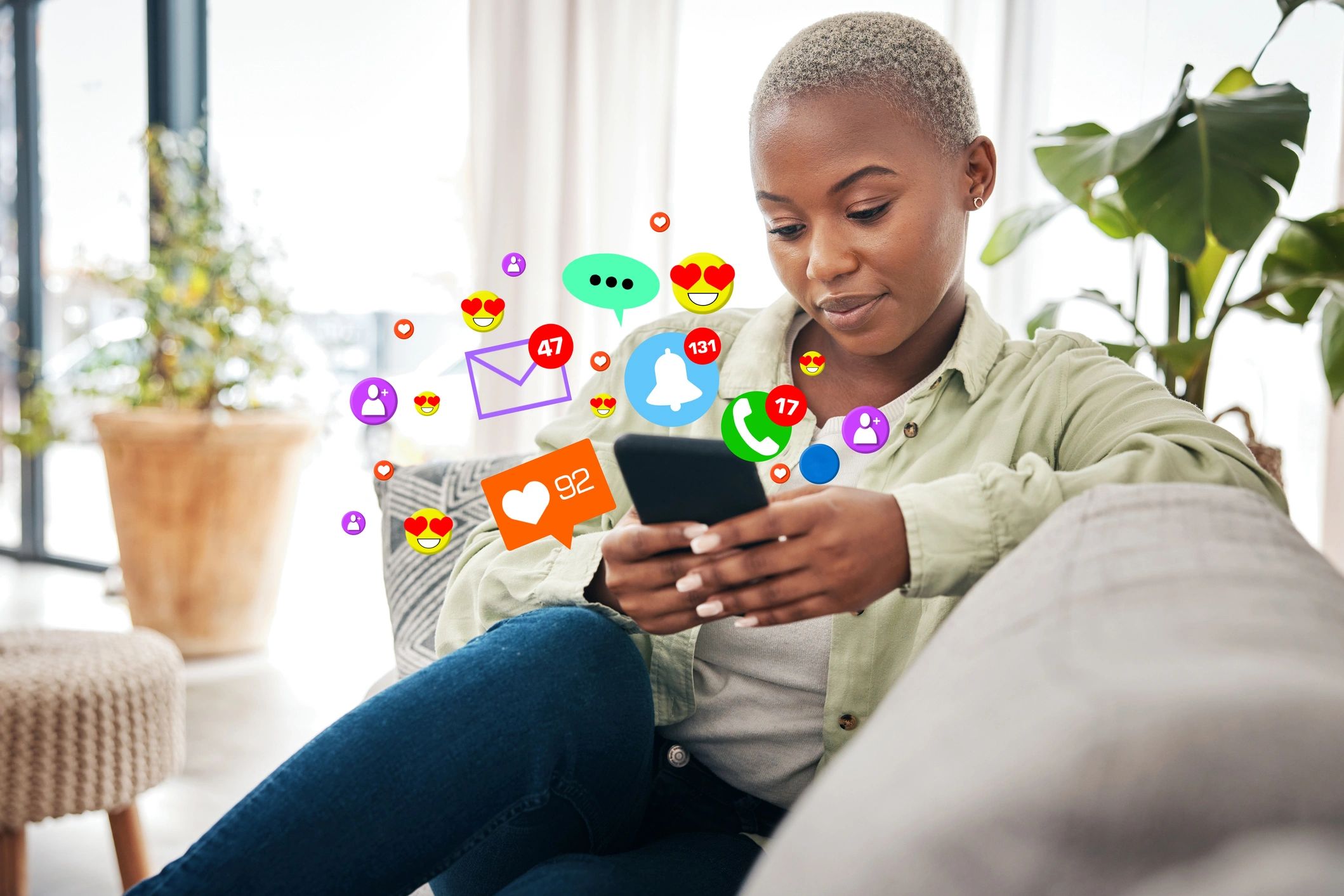Black woman with short hair, sitting and looking at her phone. Emojis displayed around the phone.