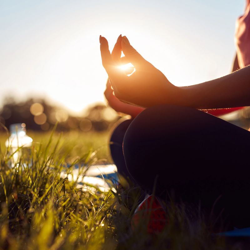 Young woman exercising on a sports yoga mat on the grass in a park during summertime sunset time.