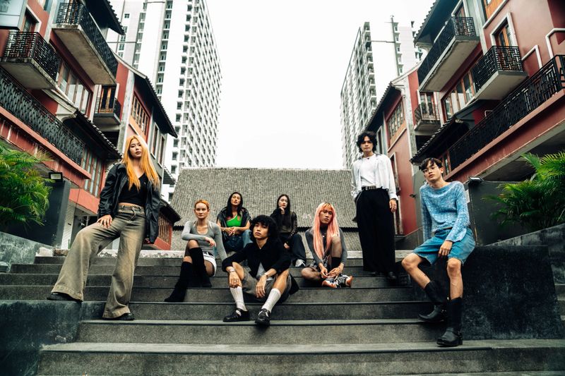 Diverse group of young adults posing confidently on city steps in trendy streetwear, capturing urban lifestyle and individuality. Perfect for themes of modern fashion and youth culture.