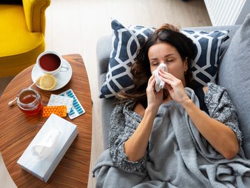 Woman blowing her nose while resting on a couch.