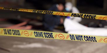Crime scene tape cordoning off an area with a covered body.