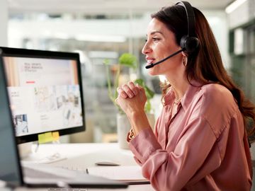 Woman in headset working at a computer in a modern office.