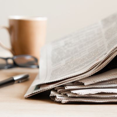 Stack of newspapers with a pen, glasses, and a coffee cup in the background.