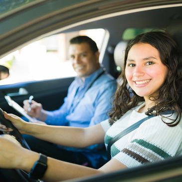 Young woman smiling while driving a car, with an instructor beside her.