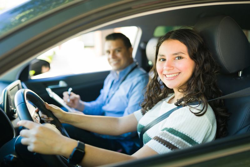 Portrait of a cheerful teenager practicing driving with her instructor taking notes during a driving lesson