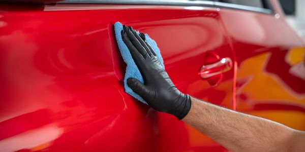 Person wearing black gloves polishing a red car with a blue cloth.
