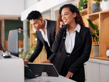 The image shows a reception desk, likely in a hotel or office, with two employees.