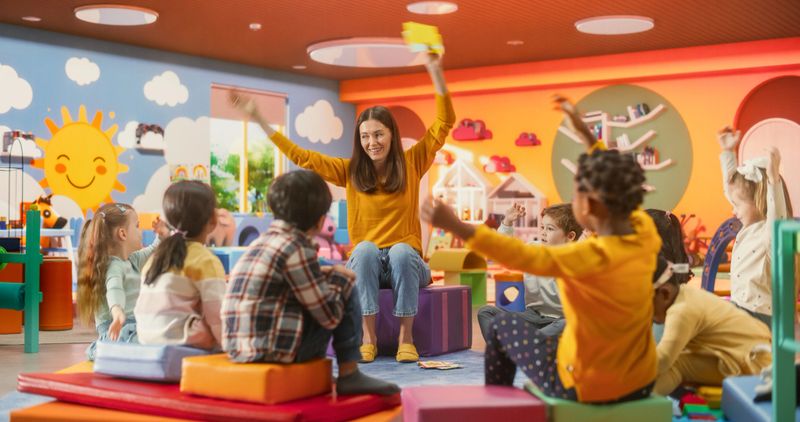 Cheerful Preschool Educator Playing, Singing and Dancing with Multiethnic Kids in Kindergarten. Small Adorable Children Learning and Having Fun