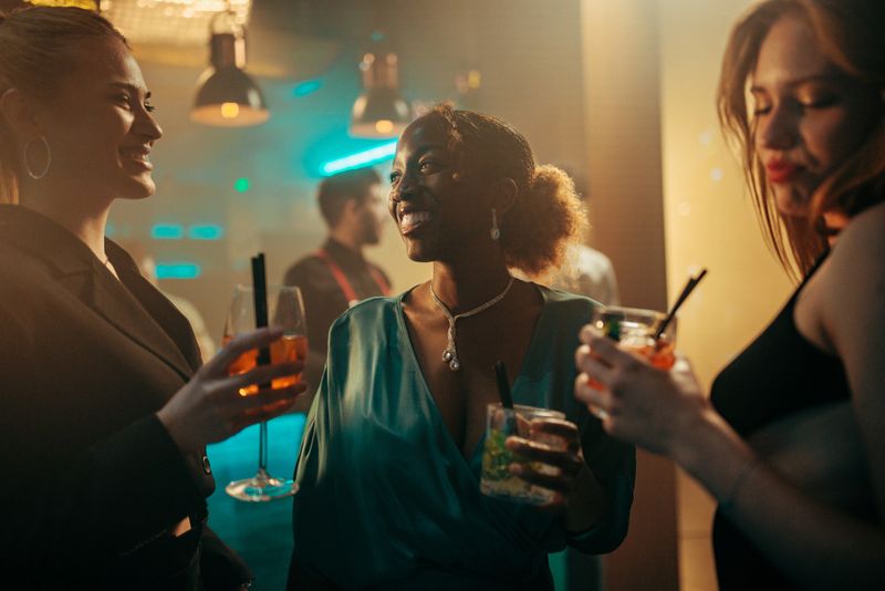 Multiracial group of female friends having fun at the nightclub, holding cocktails end enjoying the music.