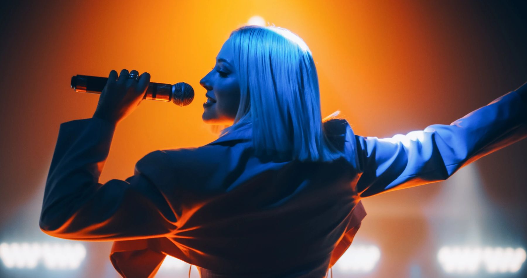 Woman singing on stage with vibrant orange and blue lighting.