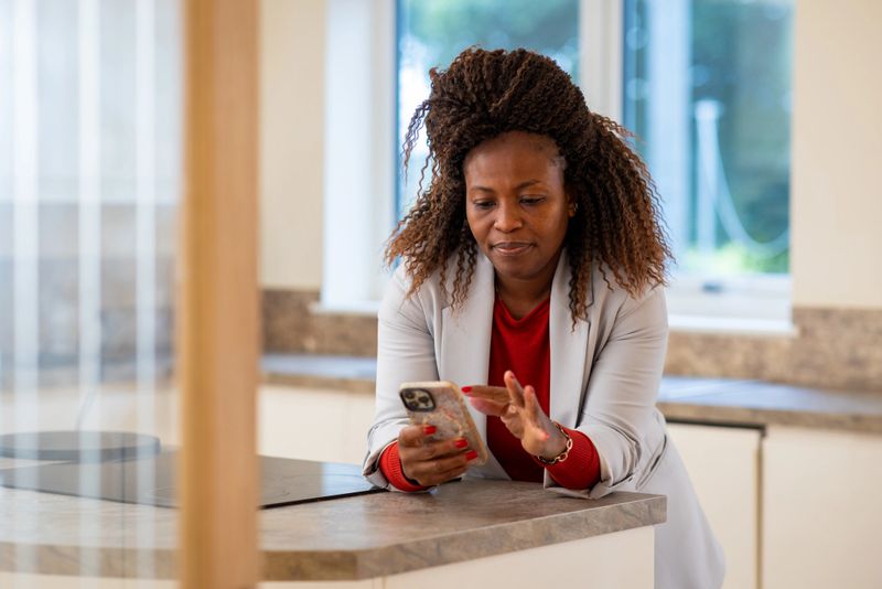 Medium shot of an estate agent leaning on the kitchen counter of a vacant property in Northumberland, North East England. She is looking down at her mobile phone with a neutral expression, wearing smart casual clothing.

Videos similar to this scenario available.