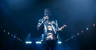 A rapper performs passionately on stage under dramatic blue lighting.