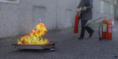 Person using fire extinguisher on flame in a tray.