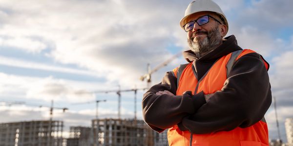 Confident construction worker in orange vest and helmet at a building site.