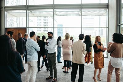 A diverse group of people networking indoors near large windows.