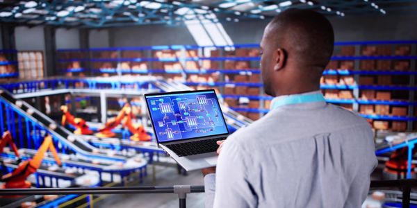 Engineer monitoring automated factory processes on a laptop inside a modern facility.