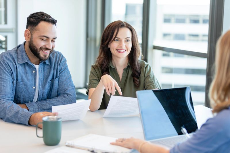 A young woman and her husband discuss a loan's terms and conditions with a bank officer.