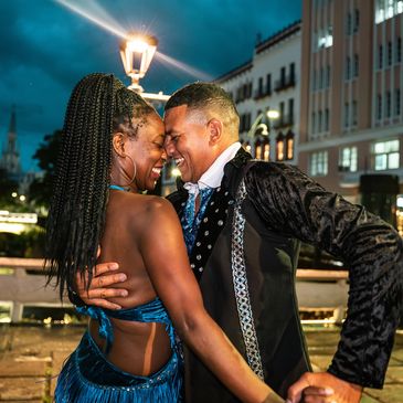 A joyful couple dancing closely at night by a river in vibrant attire.