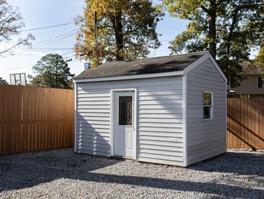 Small gray shed with a white door in a yard.
