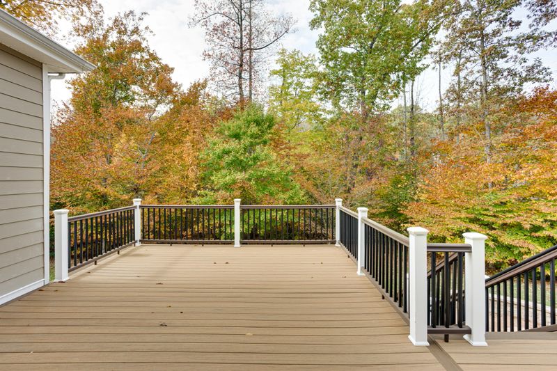 A spacious wooden deck attached to a house, bordered by a simple railing and overlooking a vibrant autumn forest, capturing the essence of tranquility and nature's beauty.