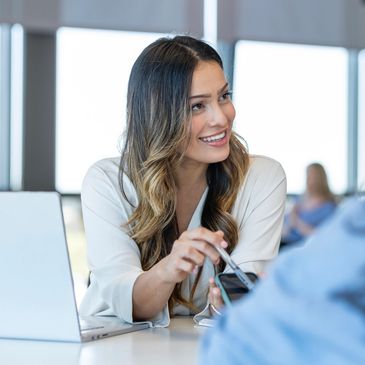 Woman smiling and showing something on her phone to a colleague in an office.