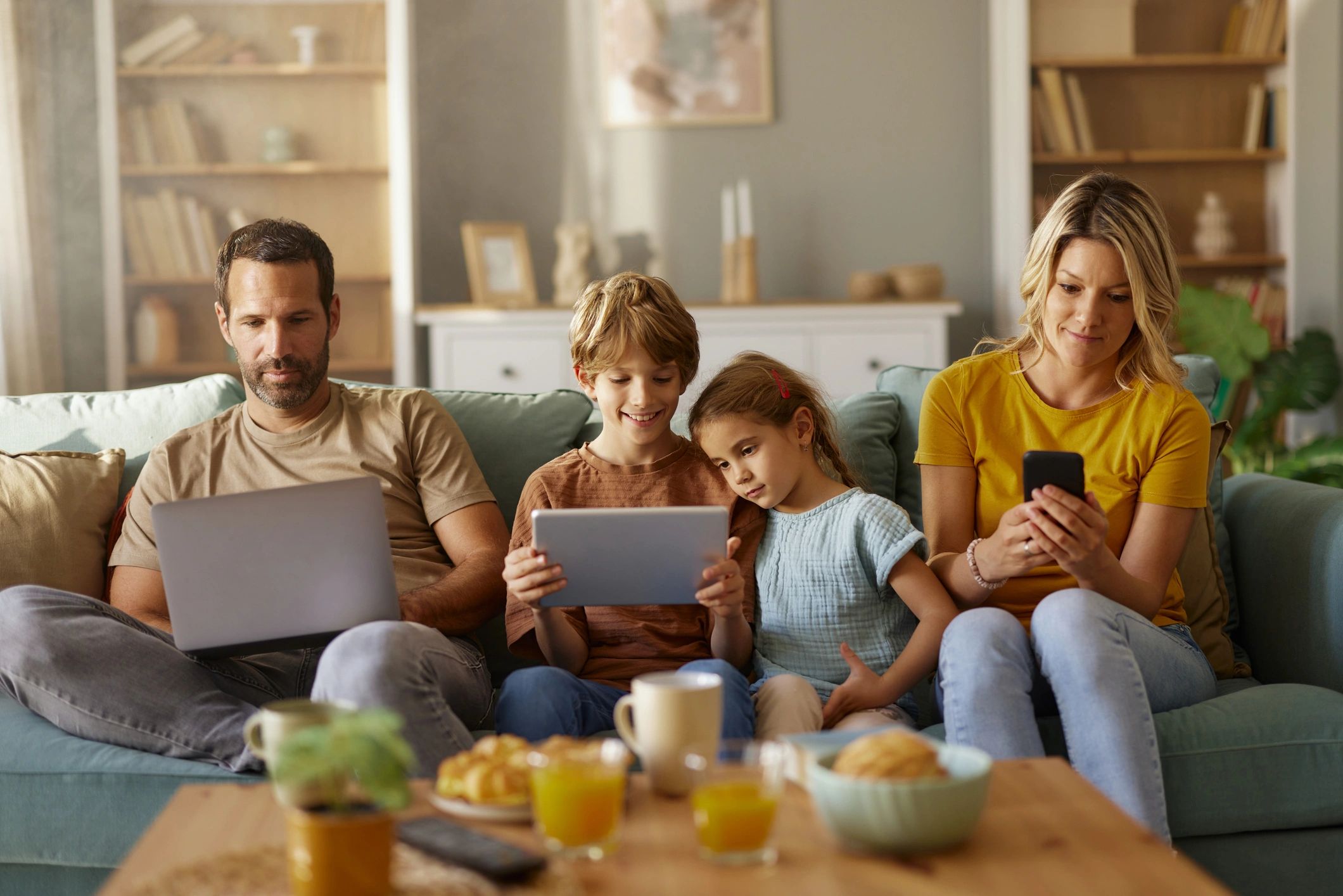 Family using digital devices together on a couch.
