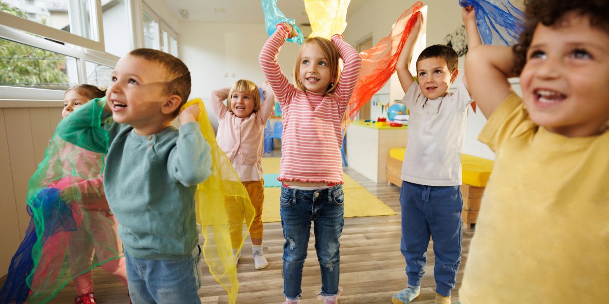 Children happily playing with colorful scarves indoors.