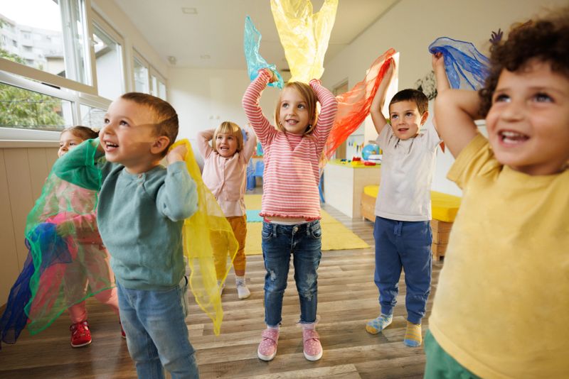 Group of happy children in playroom dance with scarves in their hands