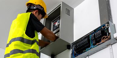 Electrician in safety gear working on an electrical panel.