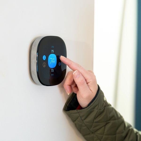 Smart thermostat mounted on a wall being adjusted in a residential property.