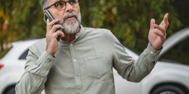 Man talking on phone with a car behind him.