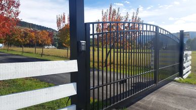 Black metal gate with keypad at a colorful autumn countryside entrance.