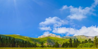 A vibrant mountain landscape under a sunny blue sky.