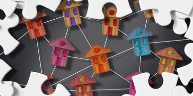 Wooden house figures connected by lines surrounded by white puzzle pieces.