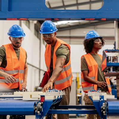 Four factory workers wearing safety gear operate machinery in ISO 9001 company